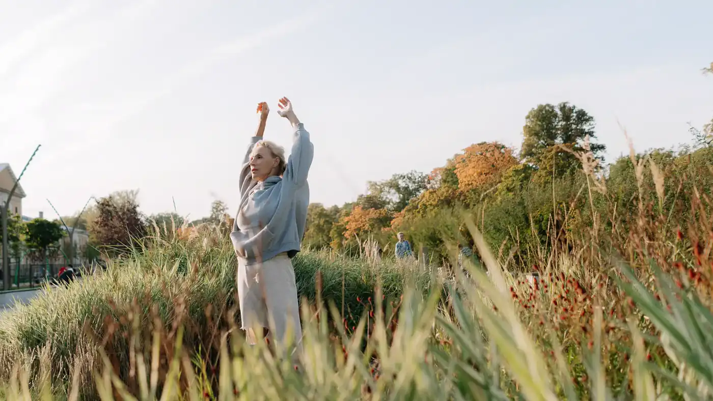Older woman raising her arms during a gentle stretch in a park