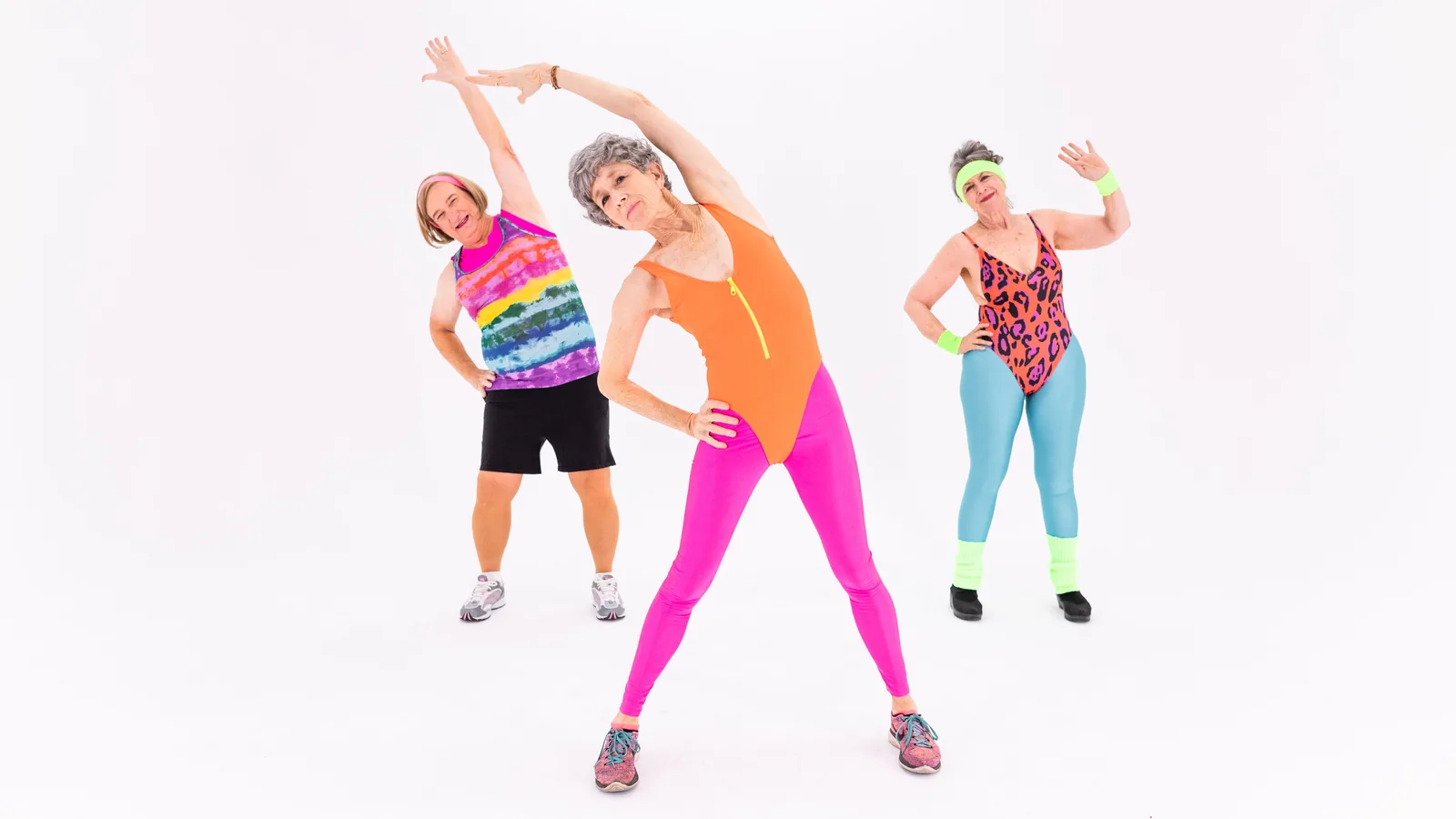 Three older women performing a standing side stretch in a studio
